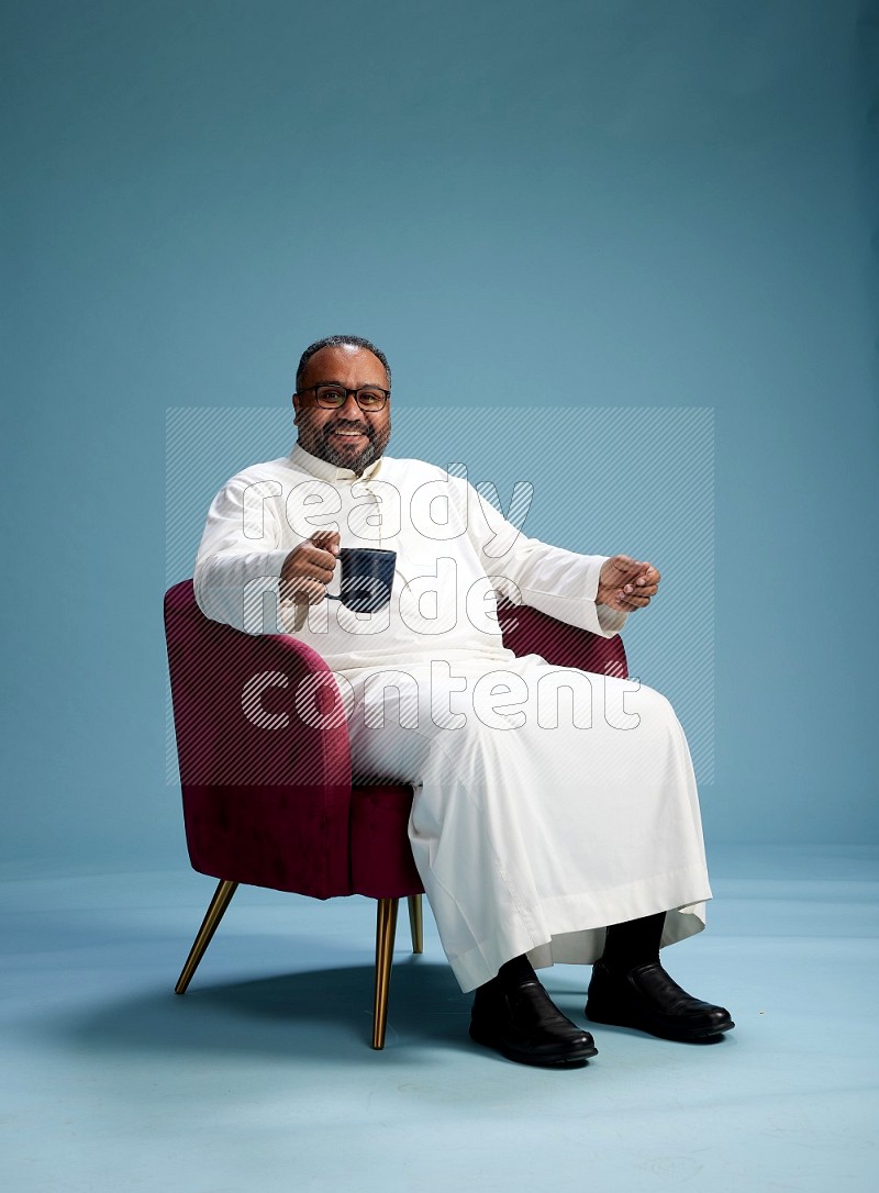 Saudi Man without shimag sitting on chair drinking coffee on blue background