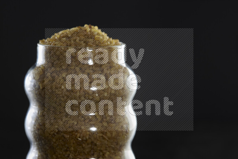 Coarse bulgur in a glass jar on black background