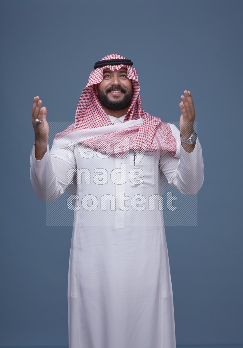 A Saudi man posing on blue background wearing Thob and Shomag