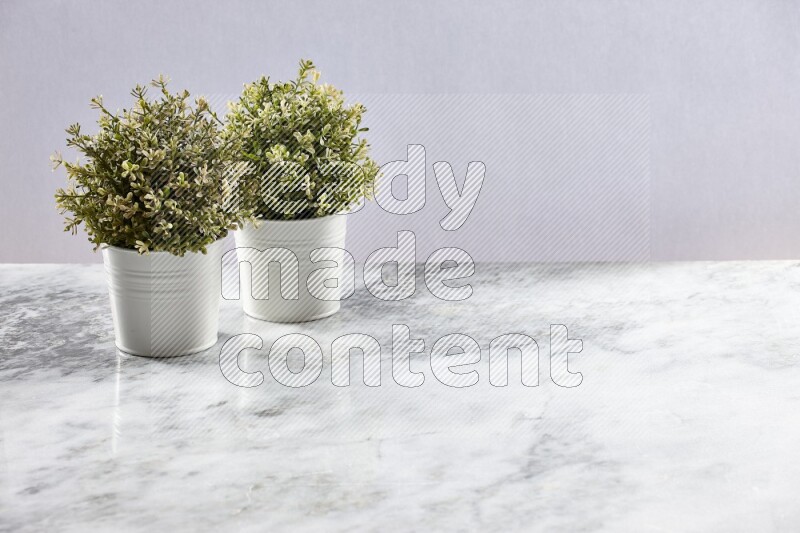 Two green artificial plants in white pot on grey marble background