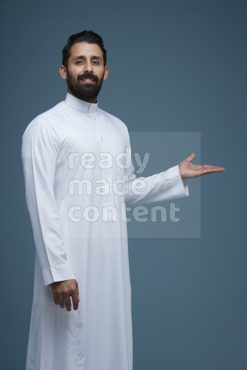 A man pointing in a blue background wearing Saudi Thob