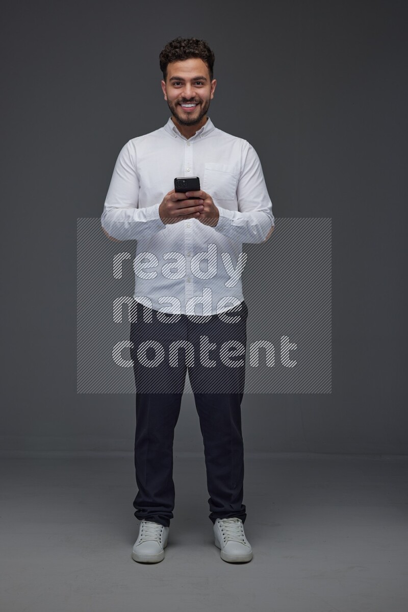 A man wearing smart casual standing and using his phone eye level on a gray background