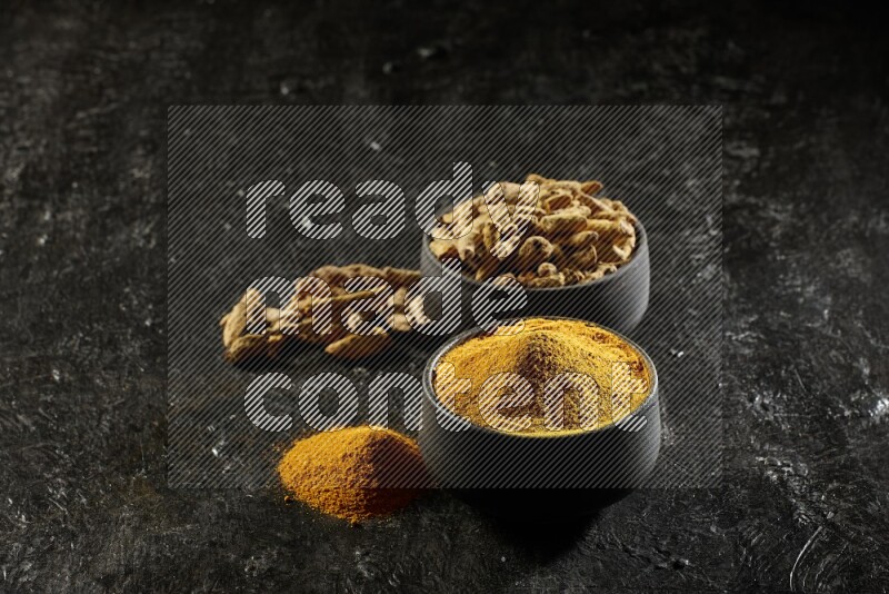 وعاءان من الفخار باللون الأسود، أحدهما ممتلئ ببودرة الكركم والآخر ممتلئ بأصابع كاملة من الكركم المجفف على خلفية سوداء