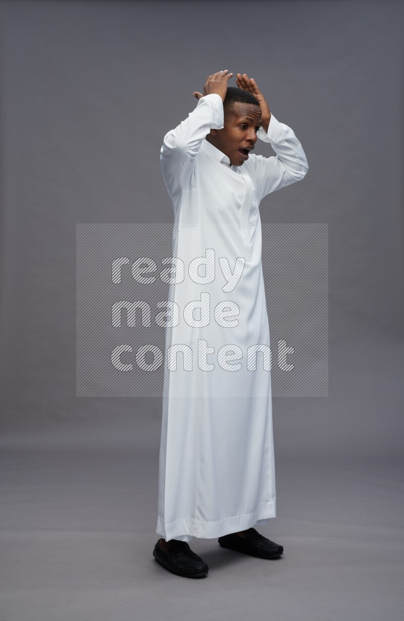 Saudi man wearing thob standing hands behind head on gray background