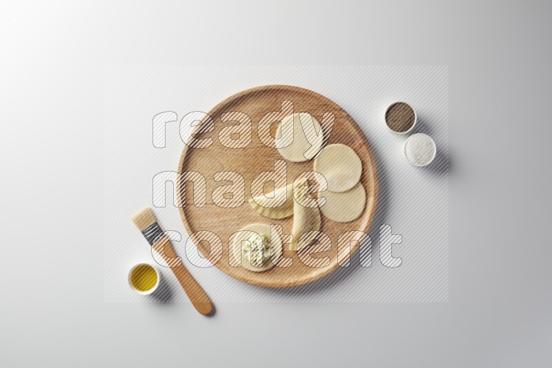 two closed sambosas and one open sambosa filled with cheese while salt, black pepper and oil with oil brush aside in a wooden dish on a white background