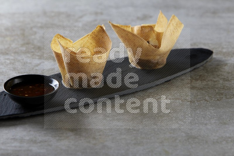 wonton cups with soy sauce ramkin on oval slate on grey textured counter top