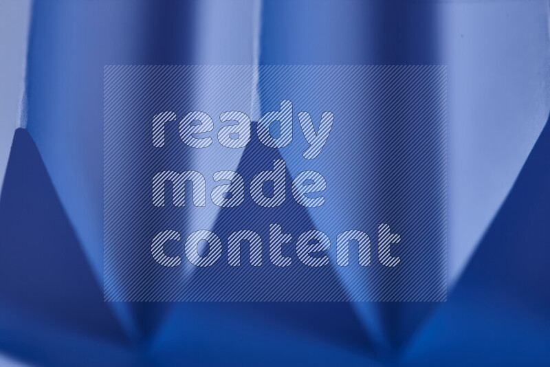 A close-up abstract image showing sharp geometric paper folds in blue gradients