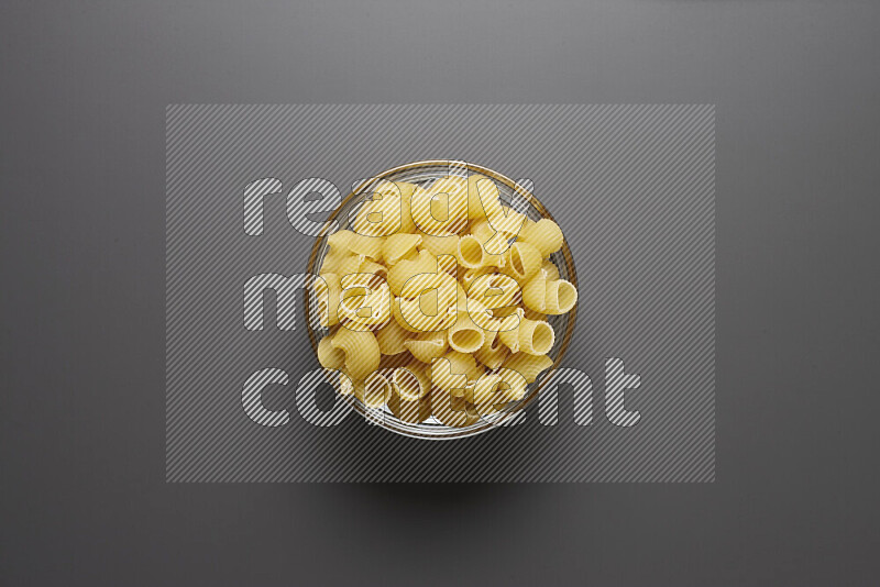 Pipe pasta in a glass bowl on grey background