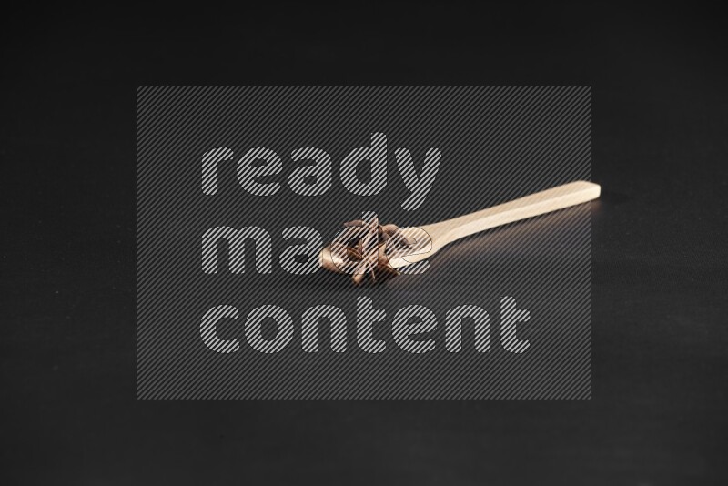 Star Anise in a wooden spoon on more stars anise filling the frame on black flooring