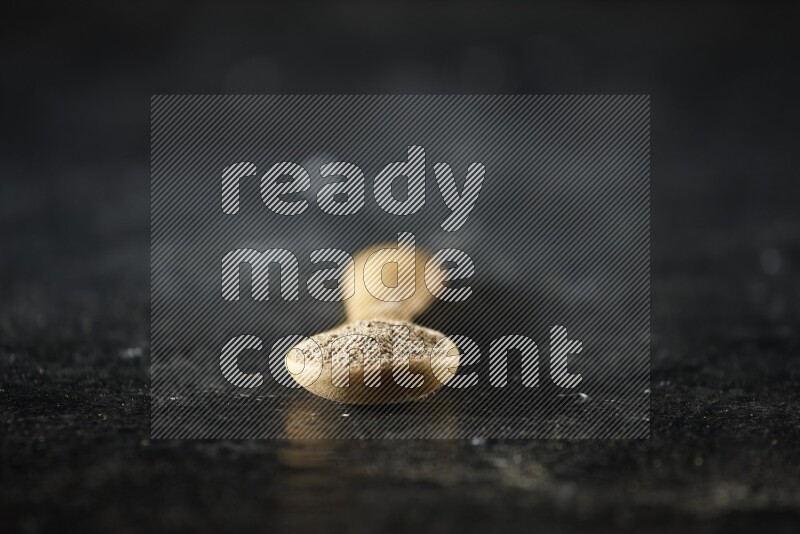 ملعقة خشبية ممتلئة ببودرة الهيل على خلفية سوداء