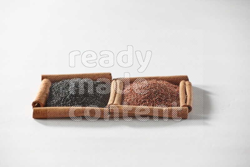 مربعان من أعواد القرفة ممتلئان بحبة البركة السوداء وبذور الكتان علي خلفية بيضاء