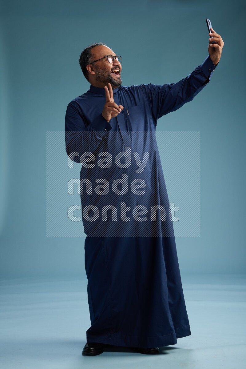 Saudi Man without shimag Standing taking selfie on blue background