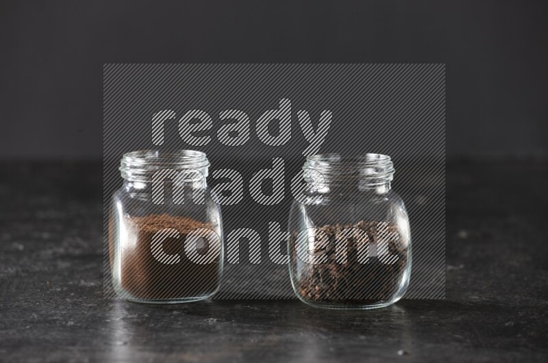 Glass spice jars full of cloves and cloves powder on textured black flooring