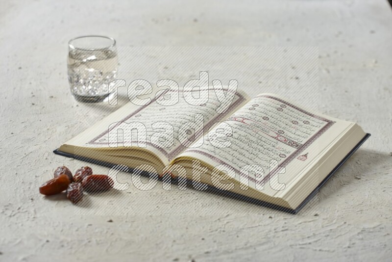 Quran with dates, prayer beads and different drinks all placed on textured white background