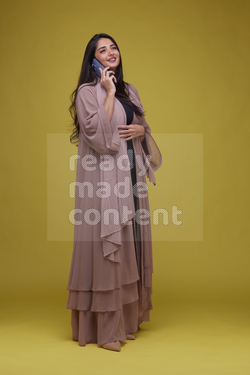 A woman Calling on a Yellow Background wearing Brown Abaya