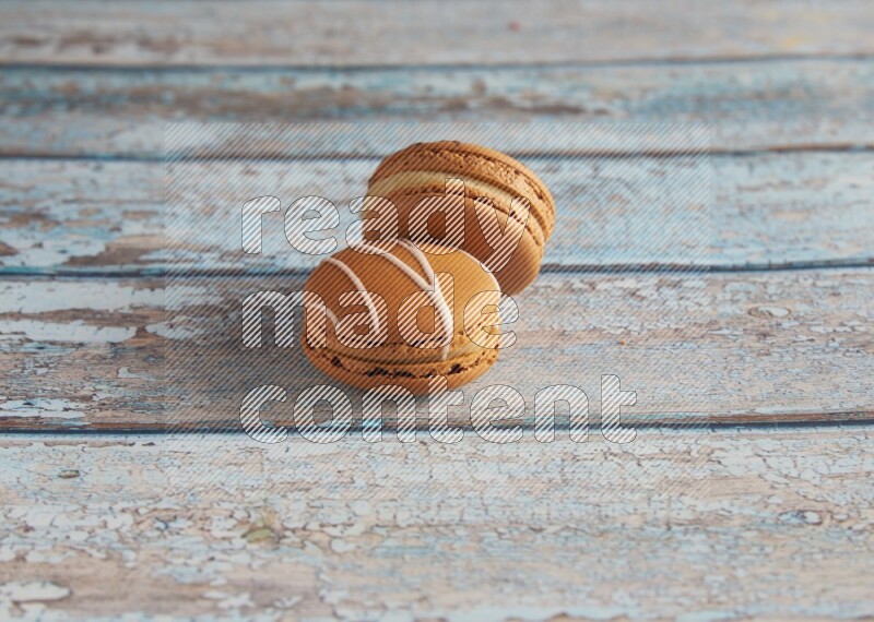 45º Shot of of two assorted Brown Irish Cream, and light brown Almond Cream macarons next to each other on light blue background