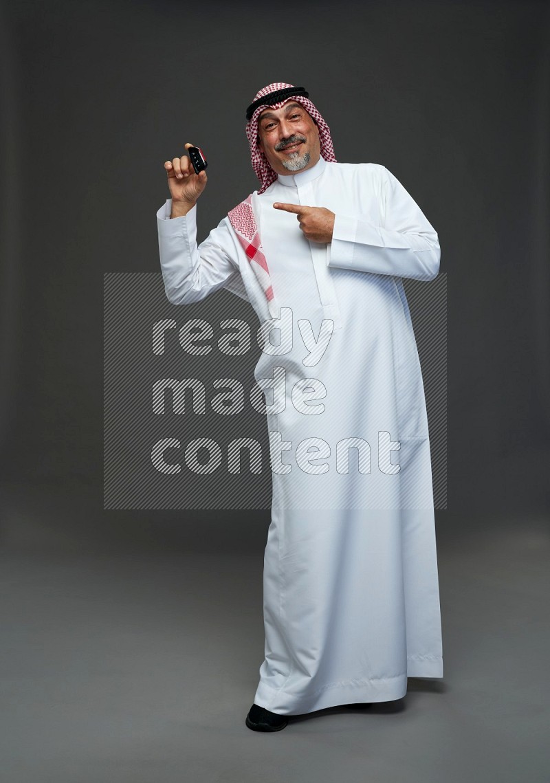 Saudi man with shomag Standing holding car key on gray background