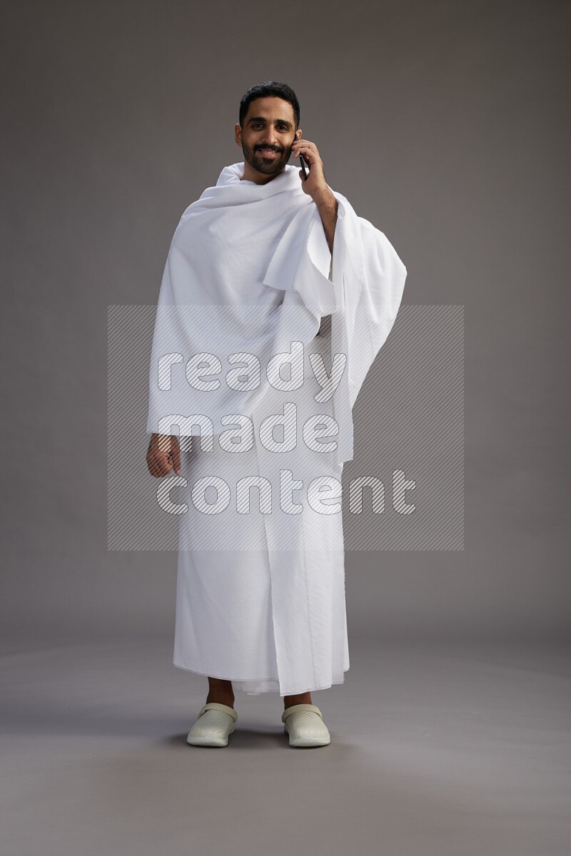 A man wearing Ehram Standing talking on phone on gray background