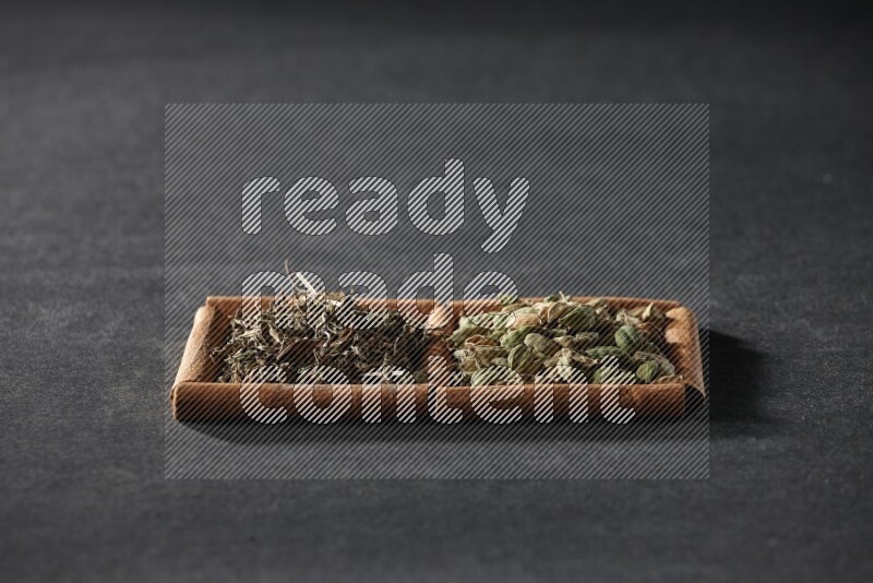 مربعان من أعواد القرفة ممتلئان بحبوب الهيل والريحان المجفف علي خلفية سوداء