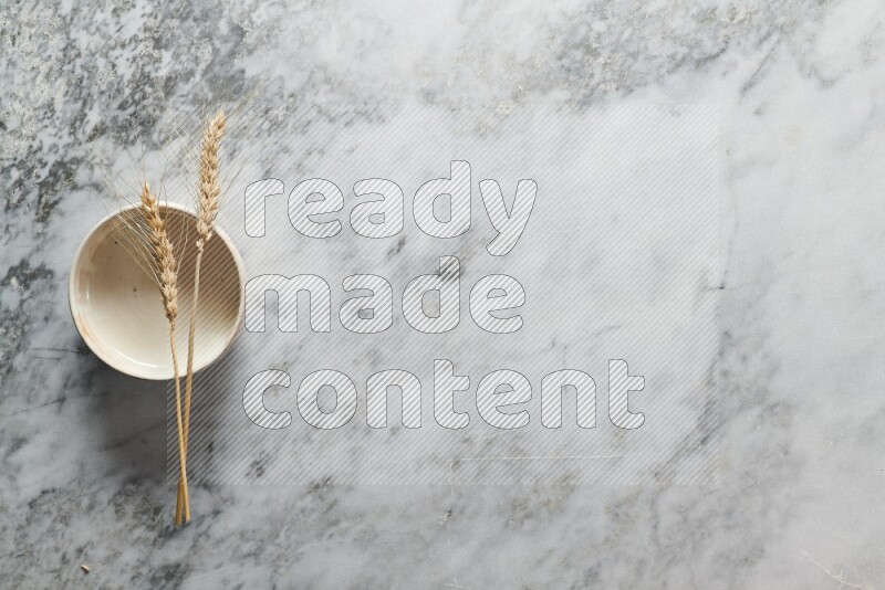 Wheat stalks on beige pottery bowl on grey marble background