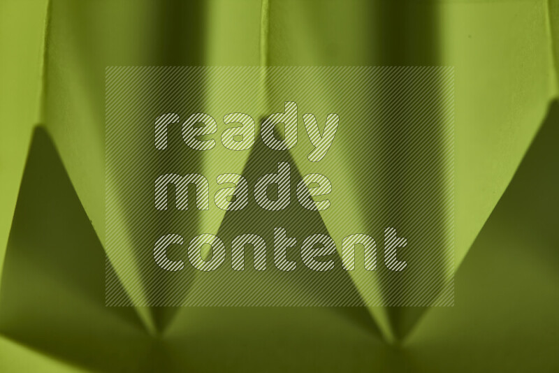 A close-up abstract image showing sharp geometric paper folds in green gradients