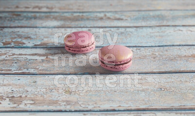 45º Shot of two Purple Strawberry macarons on light blue wooden background