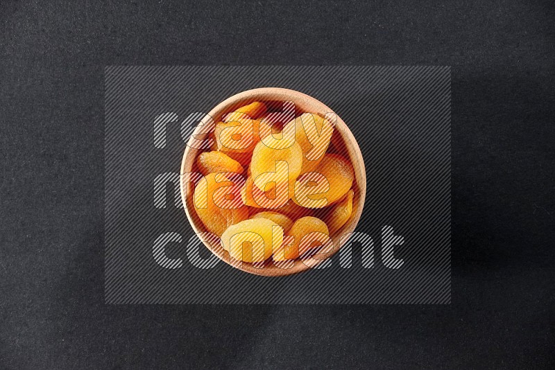 A wooden bowl full of dried apricots on a black background in different angles
