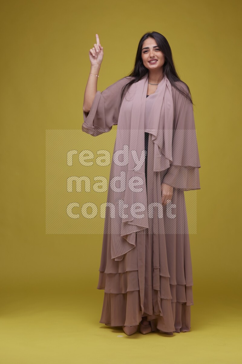 A woman Pointing on a Yellow Background wearing Brown Abaya