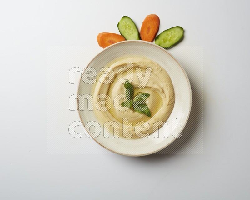 Hummus in a pottry plate garnished with mint  on a white background