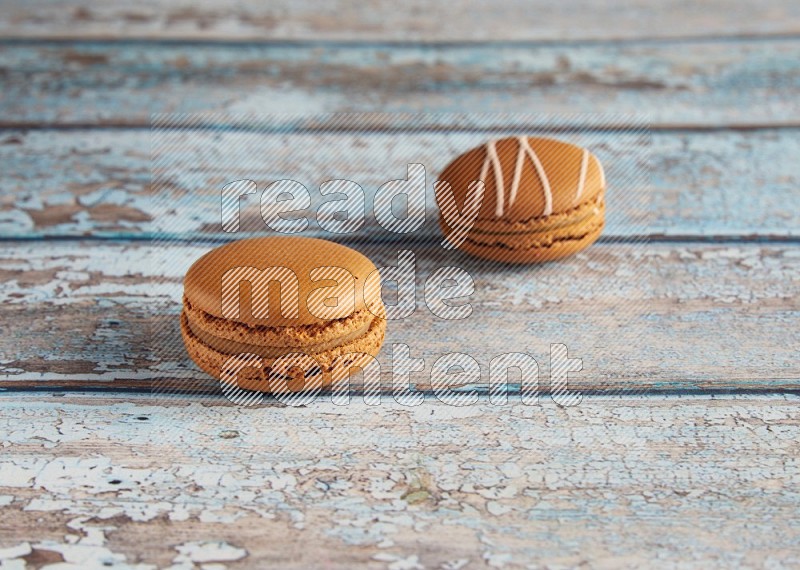 45º Shot of of two assorted Brown Irish Cream, and Brown Maple Taffy macarons  on light blue background