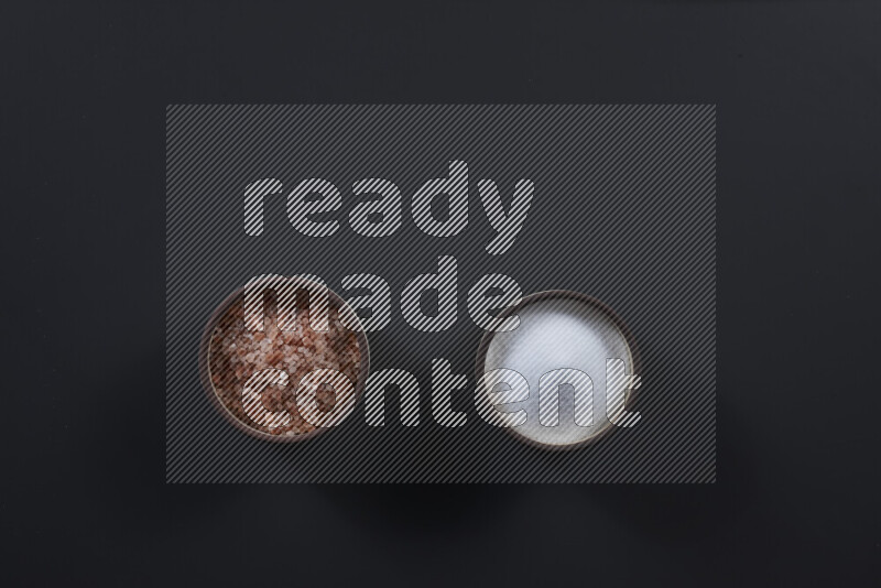 2 وعاء فخاري احدهمها ممتلئ بملح الهيمالايا والأخر بالملح الأبيض على خلفية سوداء