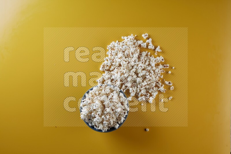 A blue pottery bowl full of popcorn with popcorn beside it on a yellow background in different angles