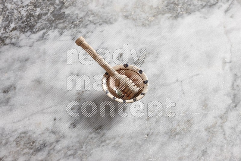 Decorative Pottery Bowl with wooden honey handle in it, on grey marble flooring, 65 degree angle