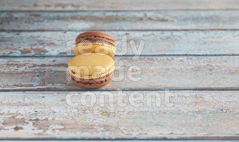 45º Shot of two Yellow and Brown Chai Latte macarons on light blue wooden background