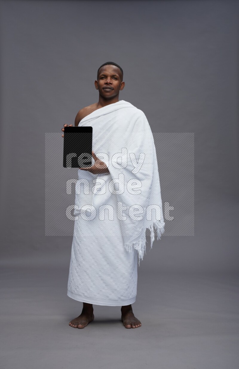 A man wearing Ehram Standing showing tablet to camera on gray background