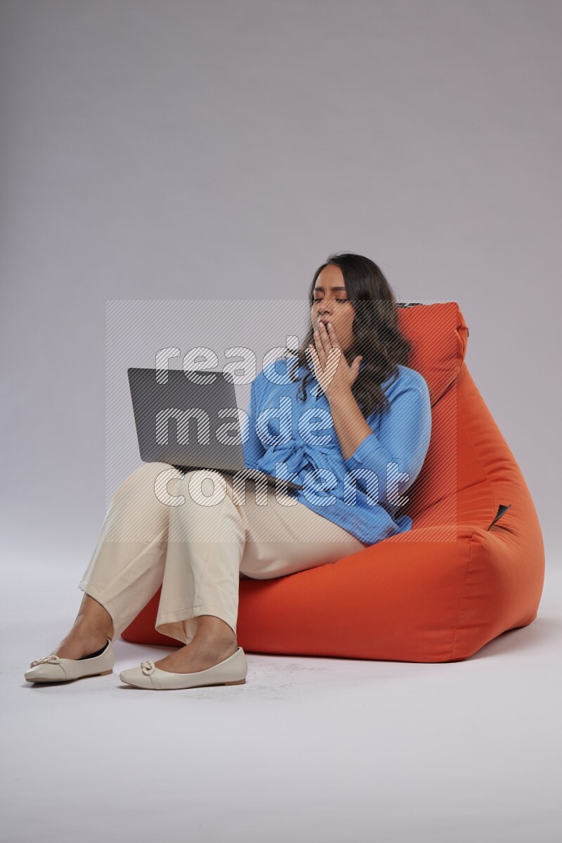 A woman sitting on an orange beanbag and working on laptop
