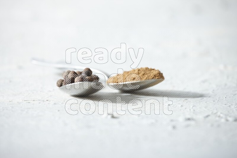 ملعقتان معدنيتان ممتلئتان ببودرة بهار الفلفل الحلو والحبوب على خلفية بيضاء