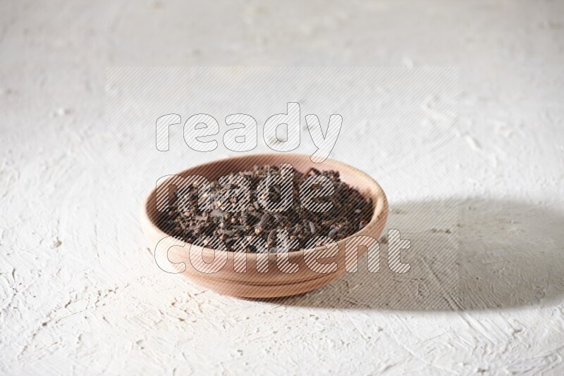 A wooden bowl full of cloves on a white flooring