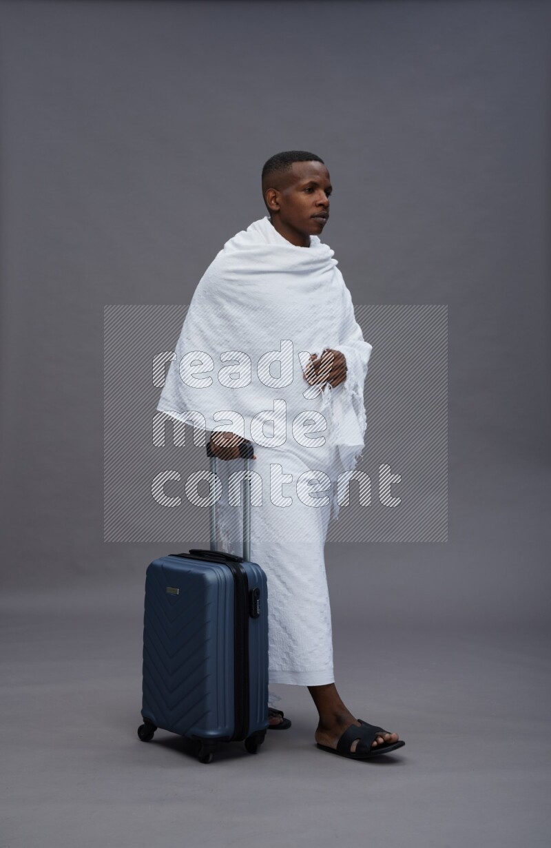 A man wearing Ehram Standing holding traveling bag on gray background