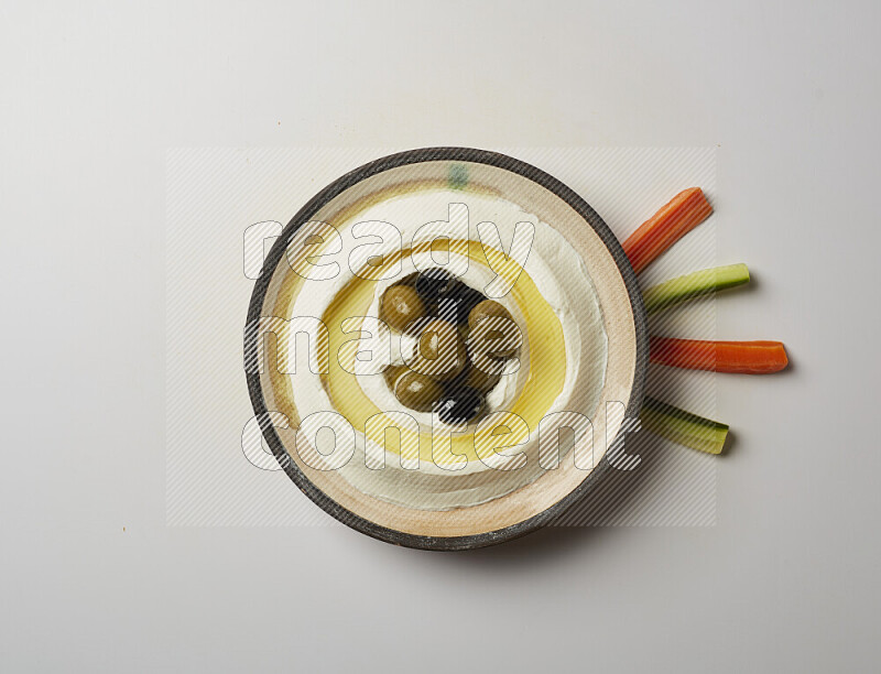 Lebnah garnished with whole black olives in a pottery plate on a white background