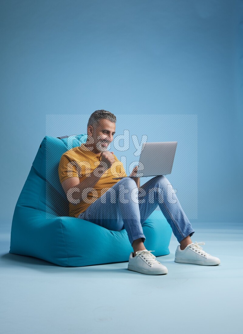 A man sitting on a blue beanbag and working on laptop