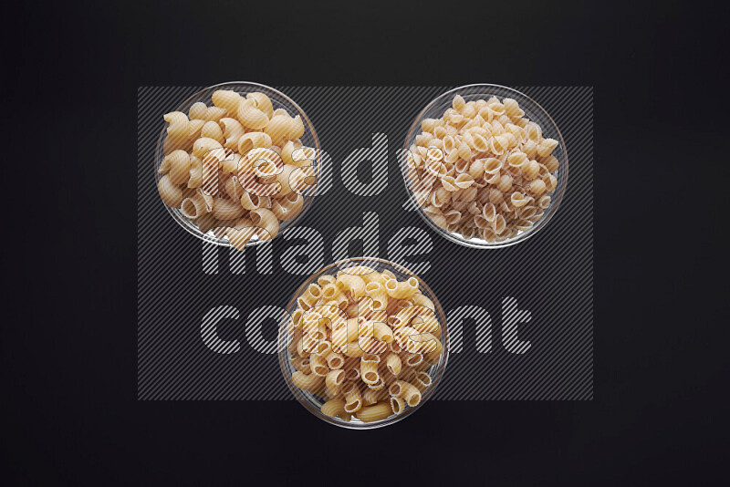 Different pasta types in glass bowls on black background