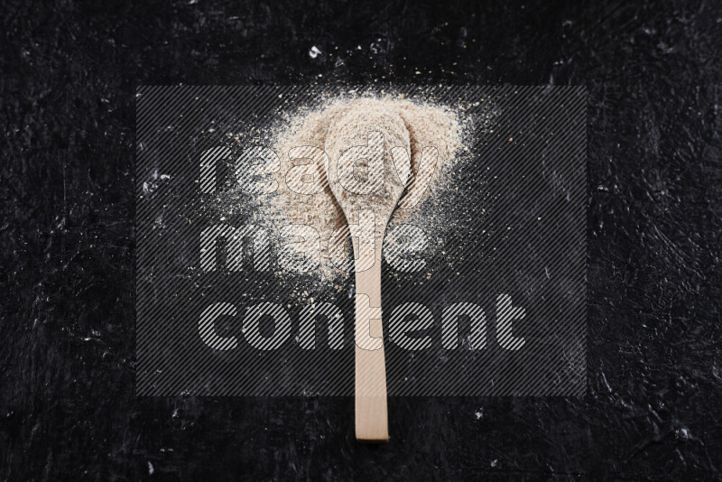 A wooden spoon full of onion powder on black background