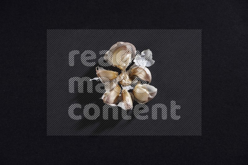 A cracked garlic bulb showing the cloves inside it on a black flooring