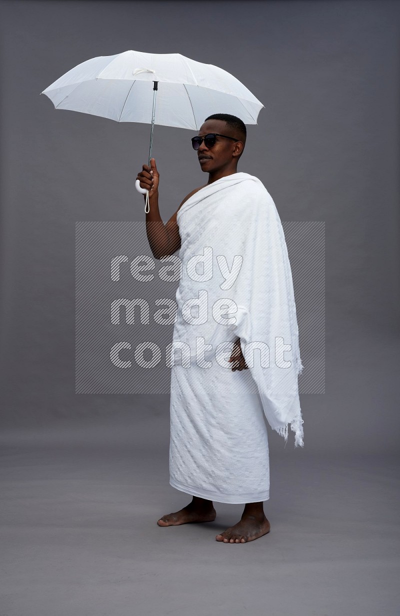 A man wearing Ehram Standing holding umbrella on gray background