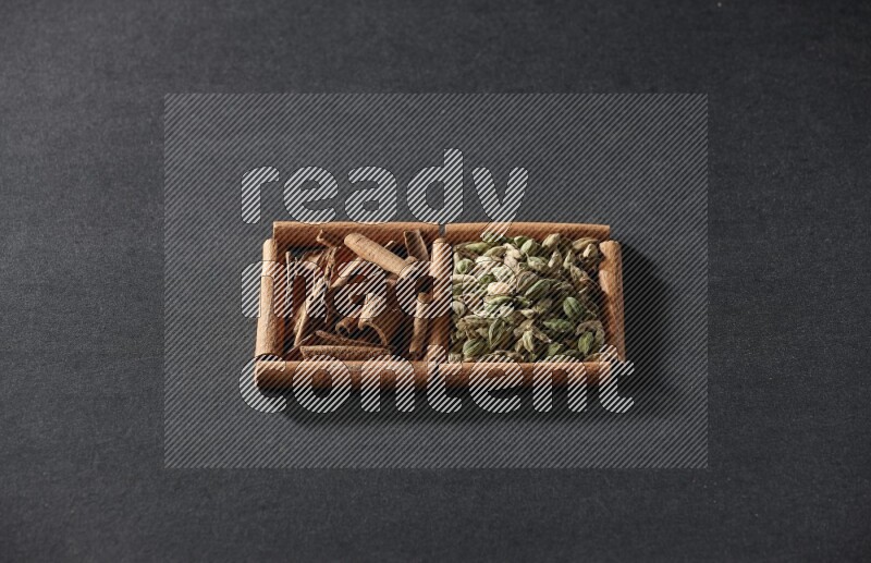 مربعان من أعواد القرفة ممتلئان بحبوب الهيل والقرفة علي خلفية سوداء