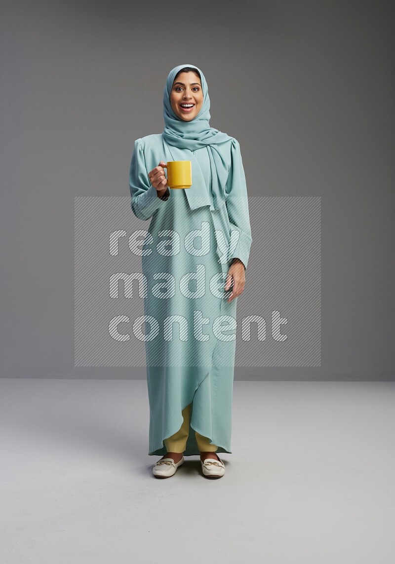 Saudi Woman wearing Abaya standing  holding a mug on Gray background