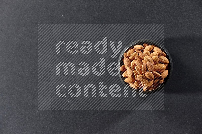 A black pottery bowl full of peeled almonds on a black background in different angles