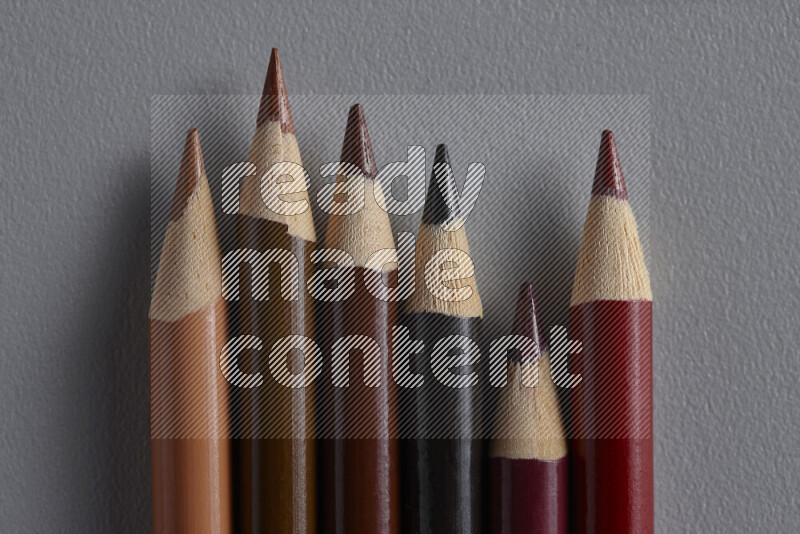 A collection of colored pencils arranged showcasing a gradient of brown hues on grey background