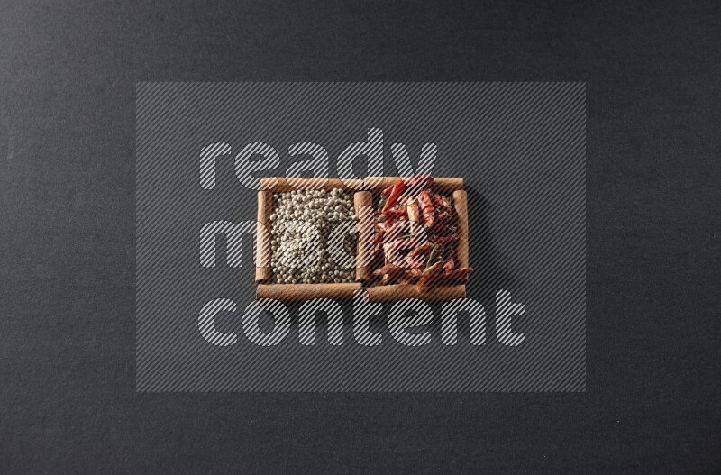 مربعان من أعواد القرفة ممتلئان بالفلفل الحار المجفف وحبوب الفلفل الأبيض علي خلفية سوداء